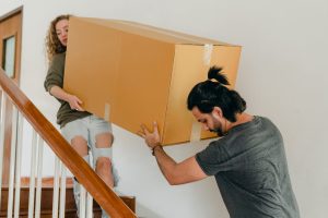 Man and woman carrying packing box down the stairs
